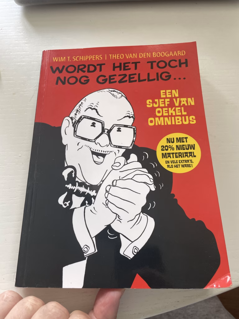 Omslag van "Wordt het toch nog gezellig - een Sjef van Oekel omnibus. Nu met 20% nieuw materiaal en vele extra's als het ware" Met een beeld van een handenwrijvende Sjef van Oekel ernaast, in zwart-wit op een rode achtergrond.